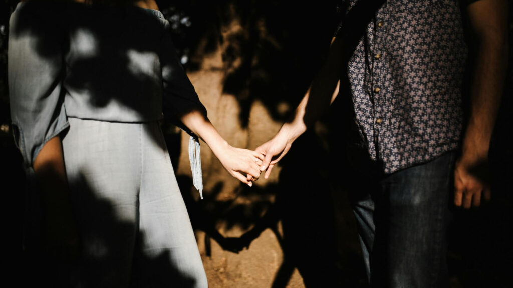 Couple holding hands tenderly, soft natural light.